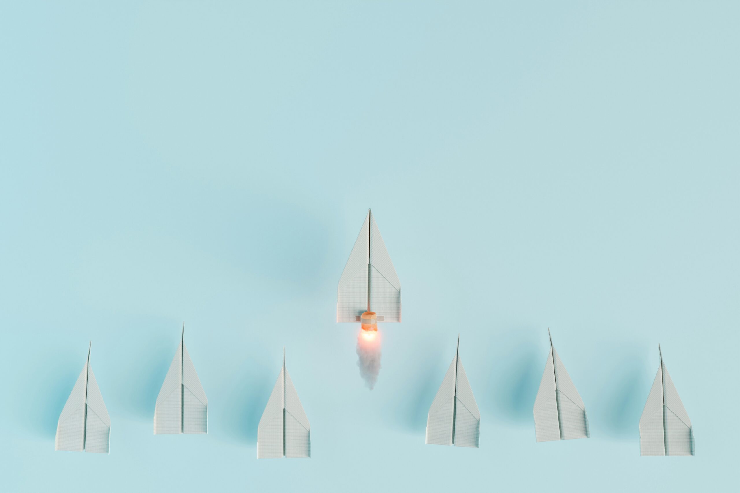 7 paper airplanes on a bright blue background. Om of the planes shoots above the rest with rocket boosters