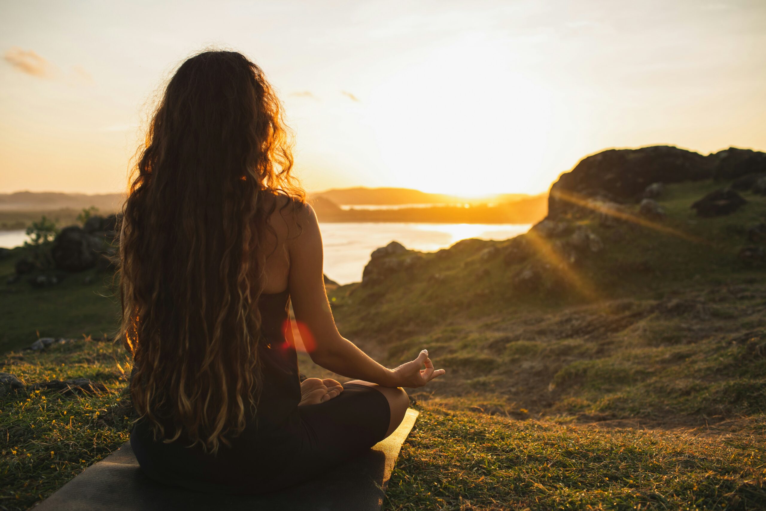 Summer solstice meditation fundraiser idea Woman practicing sunrise yoga on a hilltop overlooking water, symbolizing a peaceful start to a solstice fundraiser