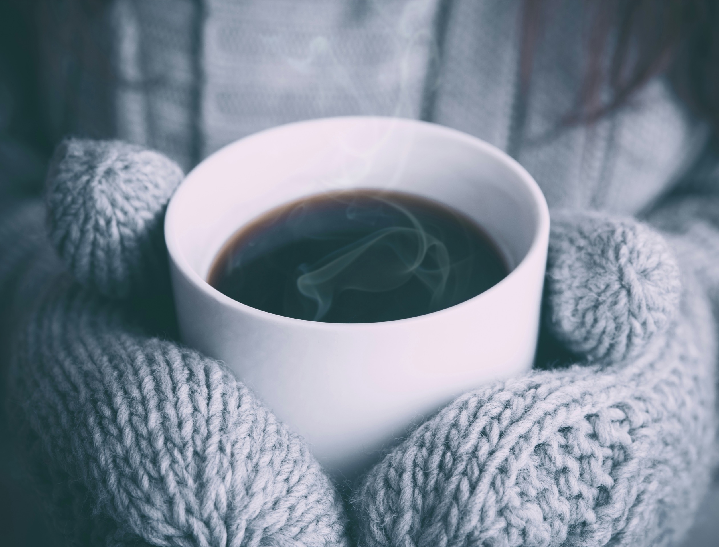 Hands in knitted mittens holding a steaming mug of coffee or hot chocolate on a cold winter day