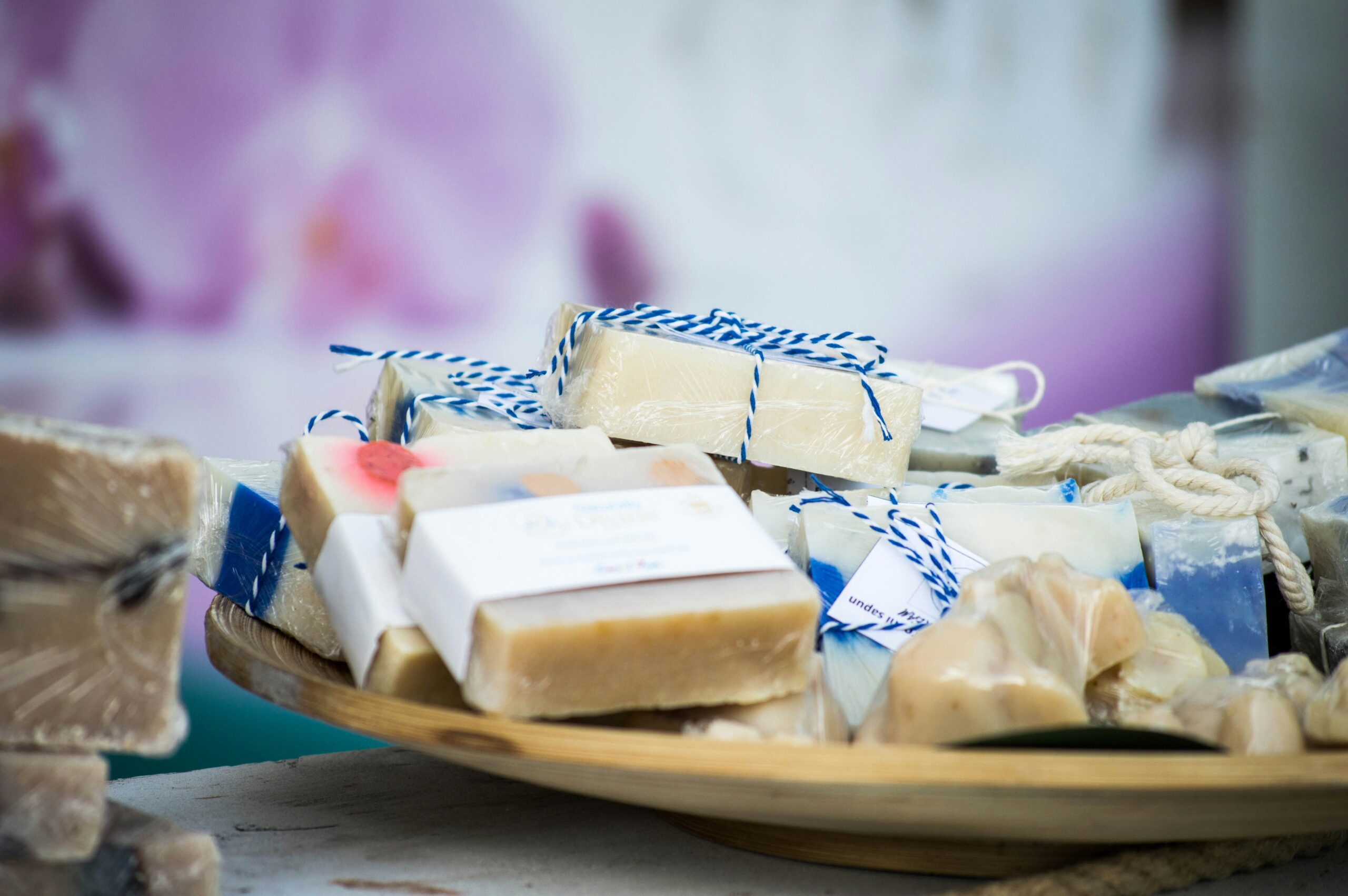Close-up of a wooden tray filled with handmade soaps wrapped in twine and labeled, displayed for sale at a makers market fundraiser.