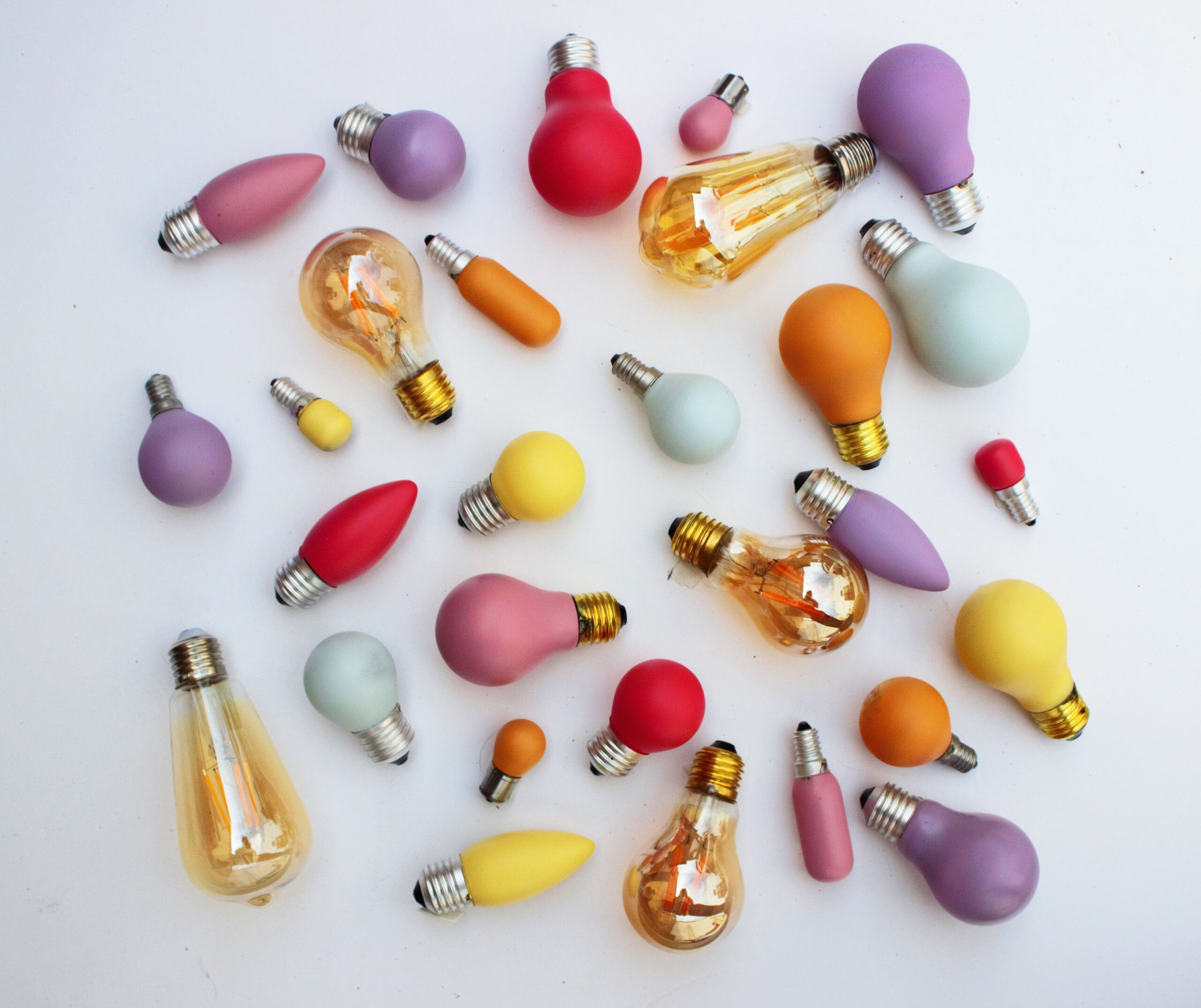 Colourful light bulbs of various shapes and sizes scattered on a white background, symbolising creative event marketing ideas.