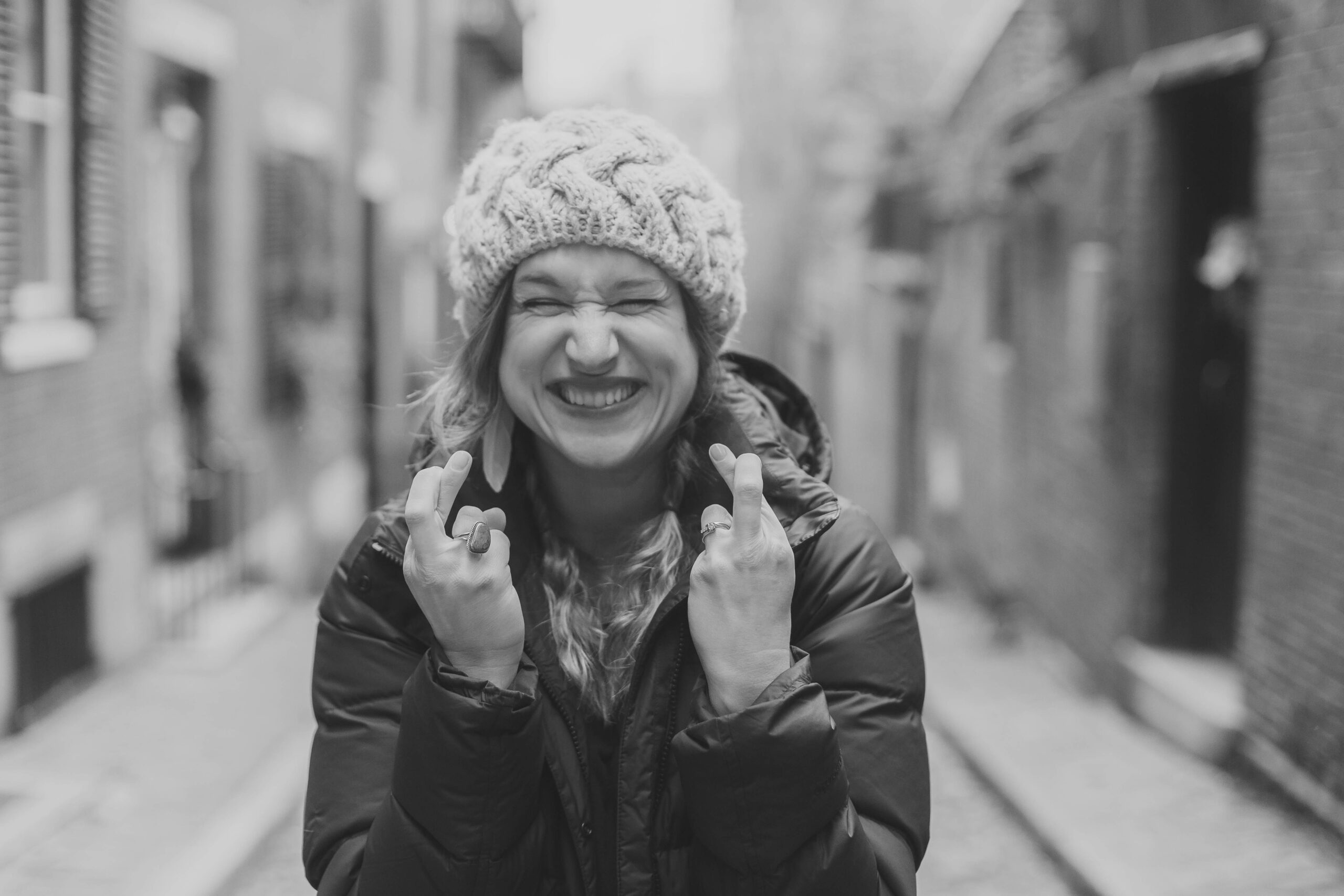 Smiling woman in winter hat crossing fingers for good luck on city street