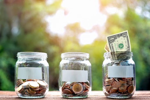 micro-donations-nonprofit-giving-jars Three glass jars filled with coins and a dollar bill, representing small donations adding up<br />
