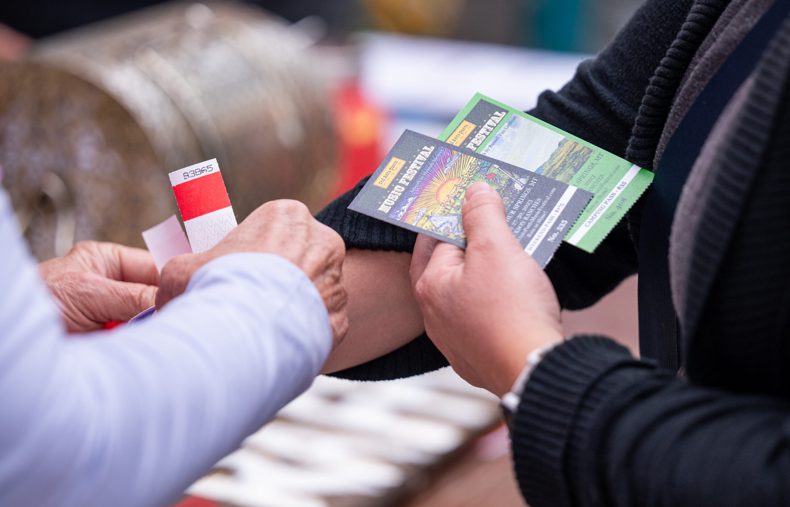 Hands exchanging printed general admission tickets and a numbered wristband at a music festival check-in gate.