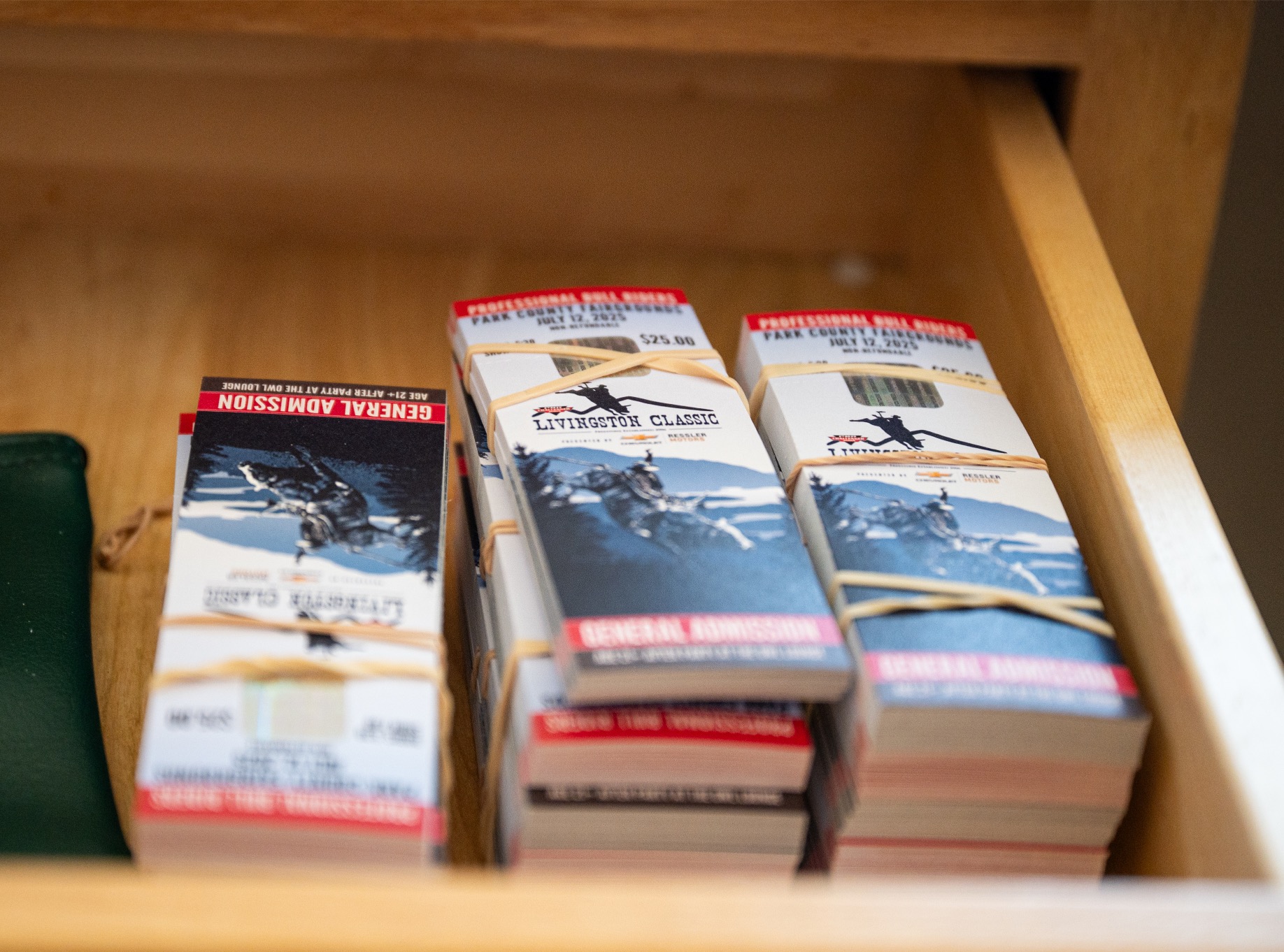 Three bundled stacks of printed general admission tickets for the Livingston Classic rodeo event, sitting in a wooden drawer at the venue.